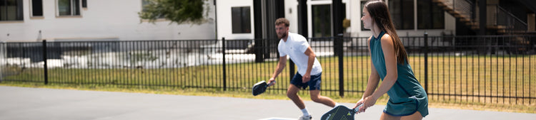 Horizontal banner image of two apparel models on a pickleball court modeling JOOLA's performance apparel.