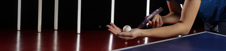 Horizontal banner image of a hand holding a table tennis racket and a table tennis ball.