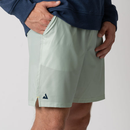 Hand in the pocket of a pair of JOOLA Men's Woven Shorts with a Seven-Inch inseam. Hushed Mint.