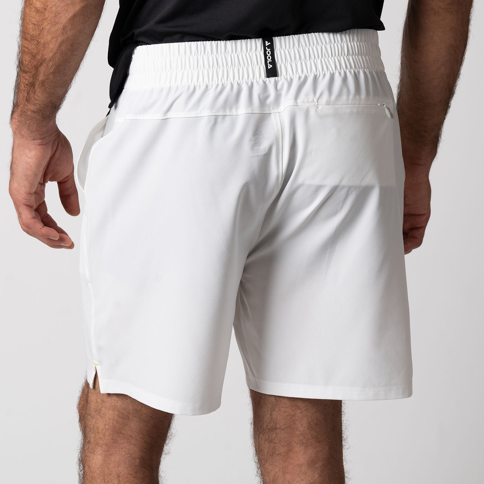 Close up image showing the branded woven pinch tab tag on the back of a pair of JOOLA Men's Woven Shorts, White.